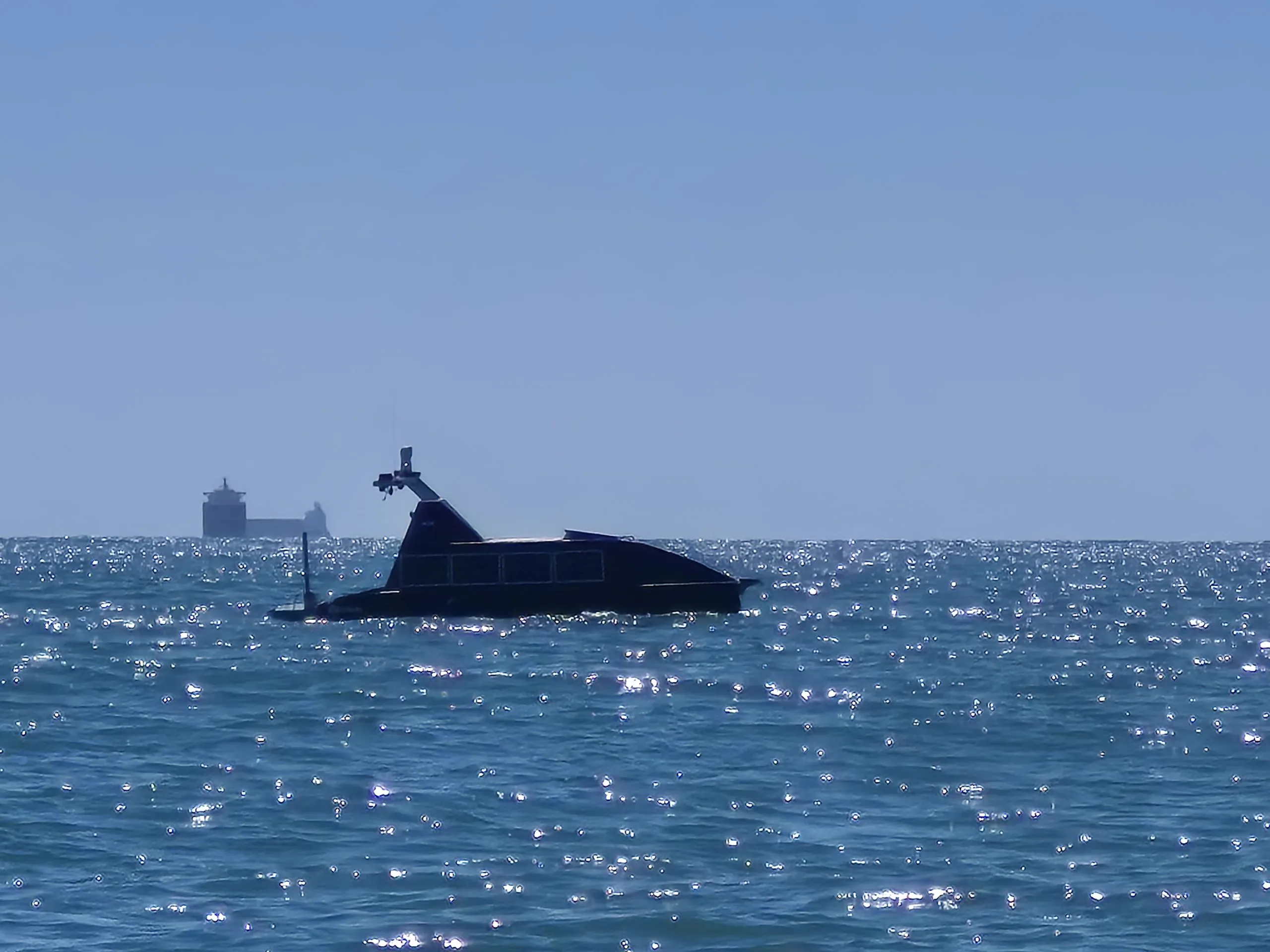 LM450 uncrewed surface vessel underway off the Port of Valencia, with a cargo ship on the horizon